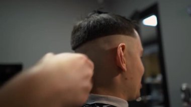 Kolunda dövme olan bir berber berber dükkanında esmer bir adamın saçını kesiyor, kırpma makinesiyle saçını kesiyor. Yüksek kaliteli görüntüler