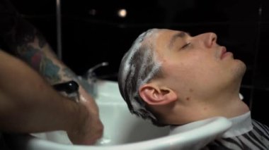 Kolunda dövme olan bir berber berber dükkanında esmer bir adamın saçını kesiyor, kırpma makinesiyle saçını kesiyor. Yüksek kaliteli görüntüler