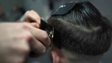 Kolunda dövme olan bir berber berber dükkanında esmer bir adamın saçını kesiyor, kırpma makinesiyle saçını kesiyor. Yüksek kaliteli görüntüler