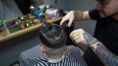 Kolunda dövme olan bir berber berber dükkanında esmer bir adamın saçını kesiyor, kırpma makinesiyle saçını kesiyor. Yüksek kaliteli görüntüler