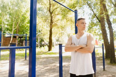 Yakışıklı şişirilmiş genç vücut geliştirici sokakta yatay bar ve paralel barlarda egzersiz yapıyor. Güzel erkek vücut şekilleri, güzellik ve sağlık, eğitim ve motivasyon. Yüksek