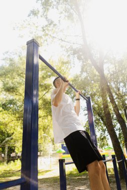 Yakışıklı şişirilmiş genç vücut geliştirici sokakta yatay bar ve paralel barlarda egzersiz yapıyor. Güzel erkek vücut şekilleri, güzellik ve sağlık, eğitim ve motivasyon. Yüksek