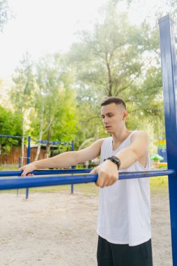 Yakışıklı şişirilmiş genç vücut geliştirici sokakta yatay bar ve paralel barlarda egzersiz yapıyor. Güzel erkek vücut şekilleri, güzellik ve sağlık, eğitim ve motivasyon. Yüksek