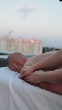 Şehirdeki bir evin çatısındaki masaj terapisti dövmeli güzel bir genç adama masaj yapıyor. Yakın plan eller cildini ve vücudunu yağlıyor. İlaç ve prosedür. Yüksek