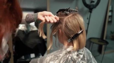 Kısa saçlı ve kısa saçlı güzel bir kız güzellik salonunda bir prosedür uyguluyor. Saç ustası müşterinin saçını boyuyor ve tonu ayarlıyor.