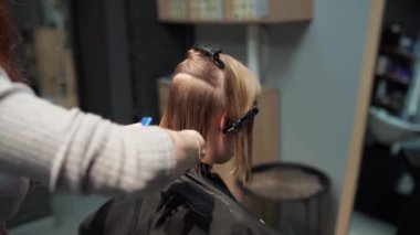 Kısa saçlı ve kısa saçlı güzel bir kız güzellik salonunda bir prosedür uyguluyor. Saç ustası müşterinin saçını boyuyor ve tonu ayarlıyor.