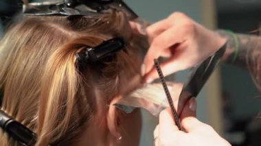 Kısa saçlı ve kısa saçlı güzel bir kız güzellik salonunda bir prosedür uyguluyor. Saç ustası müşterilere saç boyama ve tonu sunuyor. Yüksek kaliteli FullHD görüntüler