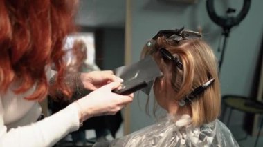 Kısa saçlı ve kısa saçlı güzel bir kız güzellik salonunda bir prosedür uyguluyor. Saç ustası müşterilere saç boyama ve tonu sunuyor. Yüksek kaliteli FullHD görüntüler