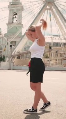 Beyaz tişörtlü güzel bir kız Kyiv 'de yazın şehir merkezinde dönme dolabın önünde poz veriyor.