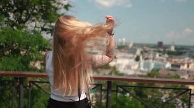 Beyaz tişörtlü genç kız gezgin yazın güneşli caddelerde yürüyor. Güzel bir kadın şehrin arka planında poz veriyor