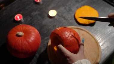 Cadılar Bayramı 'nda balkabağı parlar. Mutfaktaki kız masaya lezzetli bir portakal kabağı kesiyor. Hayalet, korku ve kutsal bayram dekoru.