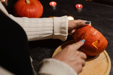 Cadılar Bayramı 'nda balkabağı parlar. Mutfaktaki kız masaya lezzetli bir portakal kabağı kesiyor. Hayalet, korku ve kutsal bayram dekoru.