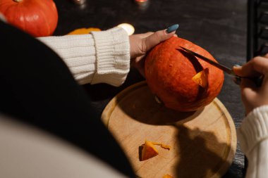 Cadılar Bayramı 'nda balkabağı parlar. Mutfaktaki kız masaya lezzetli bir portakal kabağı kesiyor. Hayalet, korku ve kutsal bayram dekoru.