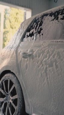 Erkek sürücü, oto yıkamada bir bez parçasıyla arabasını yıkıyor.