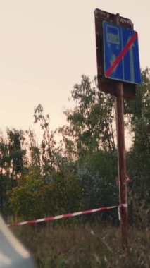 Şehrin dışında park etmiş beyaz bir araba. Kapalı bir yolda, ormanda bir tabelanın yanında. Şehrin çok dışında, çevre yolunda yarışıyor