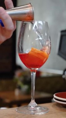 Barmen barda kokteyl bardaklarında Aperol ile birlikte bir bardak köpüklü şarap doldurur. Kokteyl Aperol Spritz. Buzlu portakal dilimi.