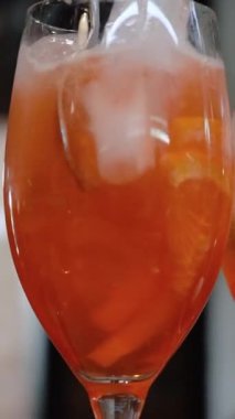 Barmen barda kokteyl bardaklarında Aperol ile birlikte bir bardak köpüklü şarap doldurur. Kokteyl Aperol Spritz. Buzlu portakal dilimi.