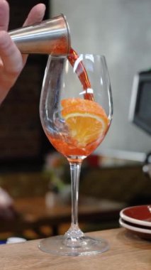 Barmen barda kokteyl bardaklarında Aperol ile birlikte bir bardak köpüklü şarap doldurur. Kokteyl Aperol Spritz. Buzlu portakal dilimi.
