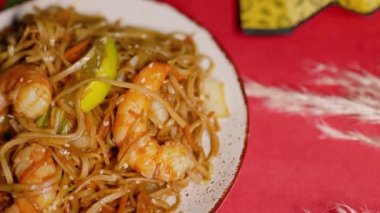 Çin Yeni Yılı. Erişteli karides ve etli Asya mutfağı. Tatil için akşam aile yemeği. Mutluluk ve iyilik için kırmızı zemin üzerinde hiyeroglifler olan altın sikkeler, yelpaze ve kartlar.