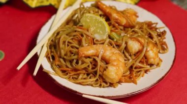 Çin Yeni Yılı. Erişteli karides ve etli Asya mutfağı. Tatil için akşam aile yemeği. Mutluluk ve iyilik için kırmızı zemin üzerinde hiyeroglifler olan altın sikkeler, yelpaze ve kartlar.