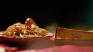 Çin Yeni Yılı. Erişteli karides ve etli Asya mutfağı. Tatil için akşam aile yemeği. Mutluluk ve iyilik için kırmızı zemin üzerinde hiyeroglifler olan altın sikkeler, yelpaze ve kartlar.