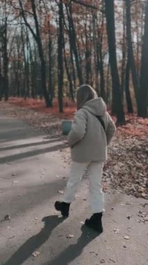 Parkta genç kız sahibiyle yürüyüşe çıkmış sevimli tüylü bir köpek yavrusu. Köpek soyu Pomeranian Spitz. Ormanda sarı sonbahar yaprakları. Yüksek kaliteli FullHD görüntüler