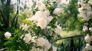 Gelin ve damadın düğün töreninden önce nehir kıyısında beyaz gül çiçeklerinin kemeri, romantik bir dekor. Yüksek kaliteli FullHD görüntüler