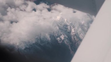 Ufuktan ve yüksek dağlardan karlı ve bulutlu bir görüntü. Seyahat ve tatil sırasında büyük bir yolcu gemisiyle gökyüzünde uçmak. Uçak penceresi ve kanadı havada. Yüksek kalite