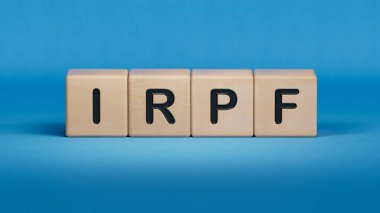 Tahta blok üzerine IRPF metni. Ahşap elementlerin kapatılması, mavi arkaplanda İşletme Konsepti 3D görüntüleme.