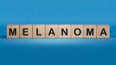 El, melanom harfinin yanına tahta bir küp koyuyor. Kelime ahşap küp üzerine yazılmıştır. Ahşap elementlere yakın plan, İş Konsepti 3D mavi arkaplan.