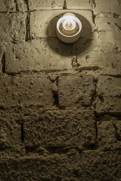 the white brick wall in the basement is illuminated by an old light bulb