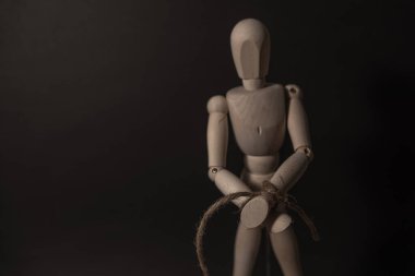 Elleri bağlı ahşap manken siyah arka planda iple bağlanmış.