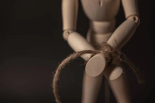 wooden mannequin with hands tied with rope on a black background
