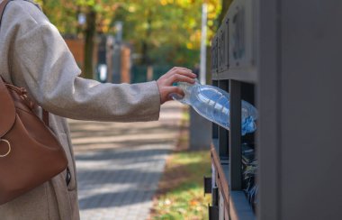Kız boş şişeyi çöpe atıyor.