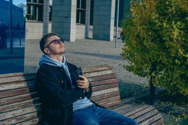 Genç bir adam parktaki bankta geçen sonbahar sıcağının tadını çıkarıyor.