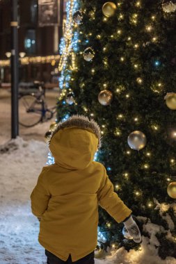 Küçük bir çocuk caddedeki Noel ağacına bakıyor.