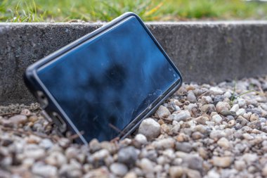 Taşlar üzerinde kırık bir ekranı olan akıllı bir telefon. Telefon ekranında hasar var. Kayıp telefon