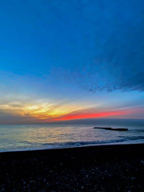 Akşamları denizin üzerinde gün batımı. Siyah kum plajı.