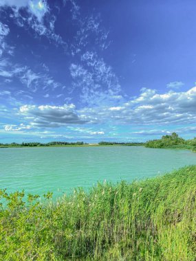 Mavi gökyüzünün altında beyaz bulutlu gölün manzarası.