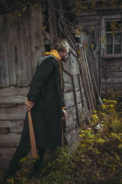 Terk edilmiş eski bir evin arka planında siyah ceketli ve maskeli bir adamın portresi.