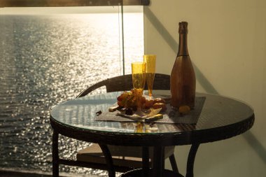 Deniz kıyısındaki masada şarap şişesi ve cam.