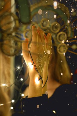 Noel ışıkları ve bokeh özgeçmişi olan genç bir kadının elleri.