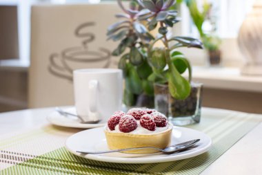 Kafedeki masada bir fincan kahve ile ahududulu tart..