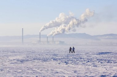 Karda yürüyen bir adam ve kadın bir elektrik santralinin önünde