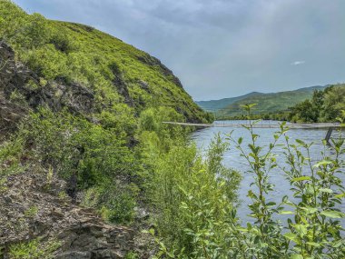 Dağ nehri manzarası ve vadinin ortasında ahşap bir köprü.