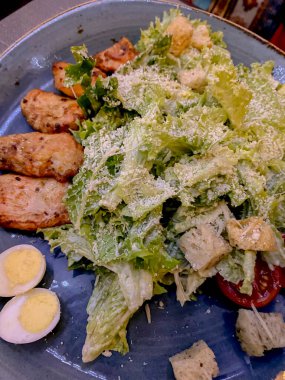 Mavi tabakta Sezar salatası, yanında da kızarmış ekmek ve domates.