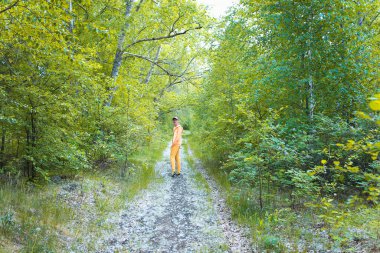 Sarı eşofmanlı genç bir adam ormanda yürüyor.