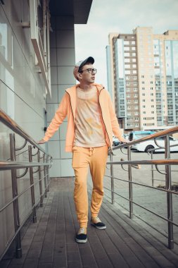 Turuncu takım elbiseli genç bir adam sokakta poz veriyor.