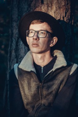Ormanda şapkalı ve gözlüklü düşünceli bir gencin portresi.