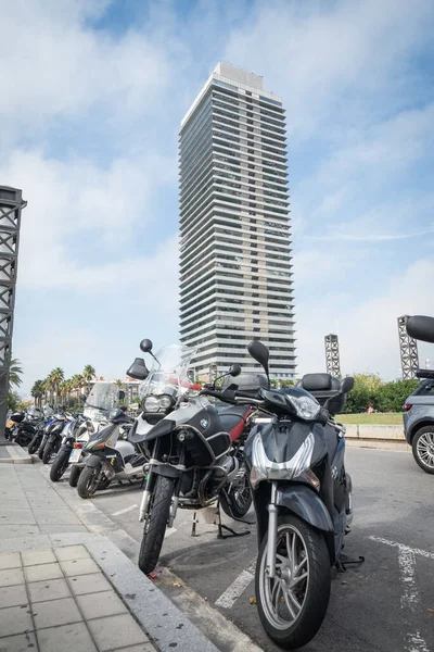 Barselona, İspanya - 11 Ekim 2015: Bir dizi scooter ve motosiklet marinanın yakınına park edilmiştir. Mapfre kulesi arka planda mavi bir gökyüzüne karşı duruyor..